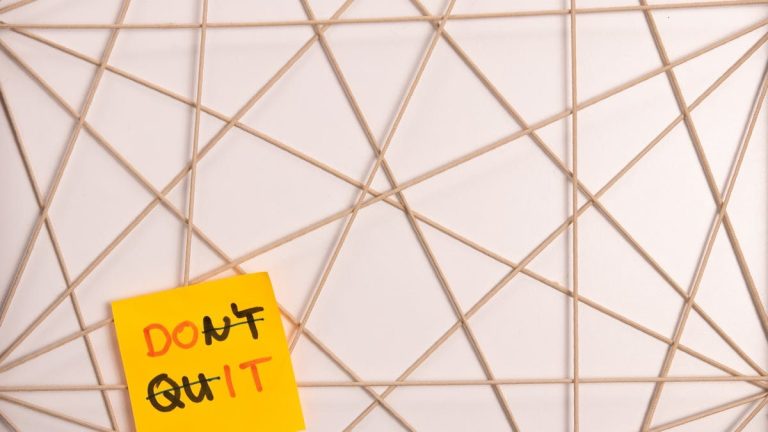Bright yellow sticky note with motivational message on an abstract geometric design background.