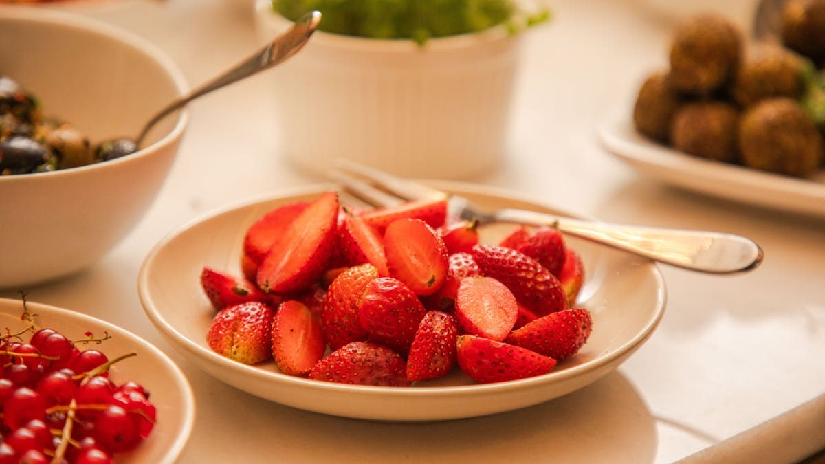 Close-up of fresh strawberries in a bowl with spoons, surrounded by various dishes.